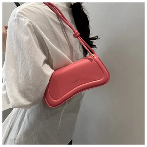 Close-up of pink crescent baguette bag with XM & BAGS logo on white pleated shirt