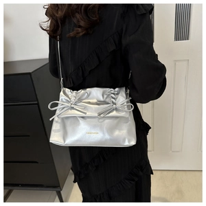 Detail of silver metallic tote bag featuring fold-over flap and bow accents on a model