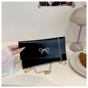 Close-up of black matte leather handbag with gold bow clasp and metal chain strap