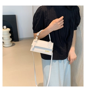 Close-up of white leather handbag with golden logo detail and elegant flap closure