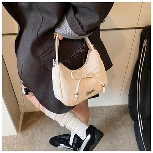 Close-up of cream bow shoulder bag with silver logo detail and textured faux leather finish