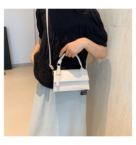 Close-up of white mini flap bag featuring a gold logo and adjustable shoulder strap