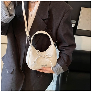 Détail d'un sac à main blanc avec nœud décoratif, texture plissée et logo métallique argenté