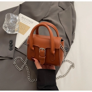 Détail du mini sac à main marron avec boucle argentée et chaîne sur une veste grise
