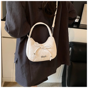 Détail du sac demi-lune blanc texturé avec nœud décoratif sur un blazer gris
