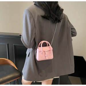 Pink mini crossbody bag with metal chain strap and top handles shown on grey blazer