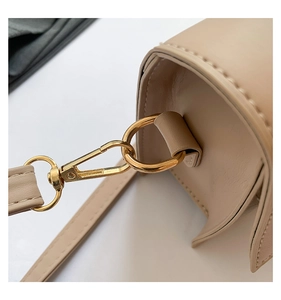 Detailed close-up of golden metal clasp and fine stitching on a beige leather handbag