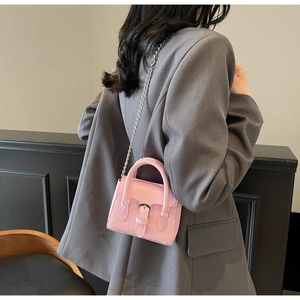 Mini sac à bandoulière rose avec chaîne argentée porté sur une veste grise