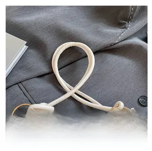 Close-up of white leather knotted shoulder strap with gold metal ring on a textured tote