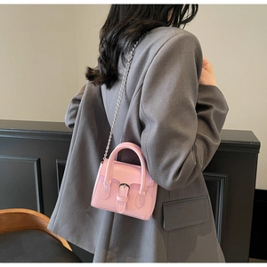 Mini sac à bandoulière en cuir mat rose avec chaîne en argent porté sur un blazer gris