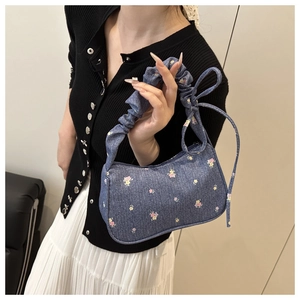 Détail de broderies florales sur sac en jean bleu avec anse à volants et nœud