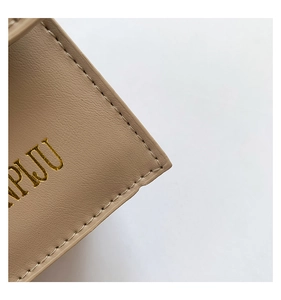 Close-up of beige leather bag featuring textured synthetic leather and gold foil logo