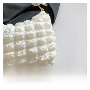 Detail of white bubble pleated fabric and gold metal ring on a soft shoulder bag