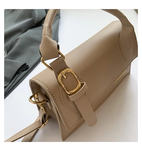 Close-up of beige crossbody bag with textured leather and polished gold metal buckles