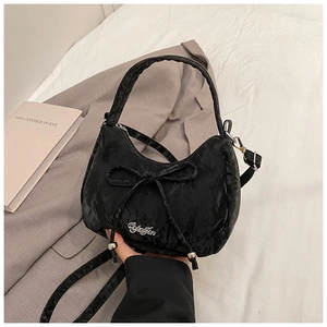 Detail of black pleated crossbody bag with ribbon bow and metal logo on soft fabrics