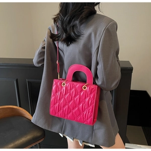 Dettaglio della borsa quadrata trapuntata rosso rosa con finiture dorate sulla modella
