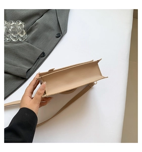 Detail view of the bottom thickness and side stitching of a beige faux leather handbag