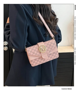 Detailed view of pink monogram crossbody bag with golden metal logo and textured finish