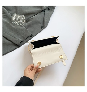 Detail of cream flap square bag showing magnetic gold buckles and inner structure