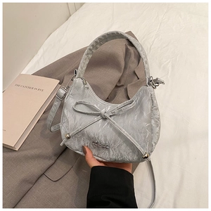 Detail of silver metallic textured underarm bag with bow decoration and metal logo