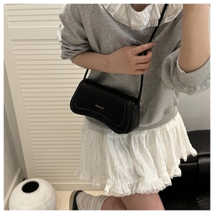 Detailed view of the black leather shoulder bag with gold logo on a female model