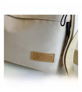 Close-up of beige canvas crossbody bag featuring a brown leather fashion logo patch