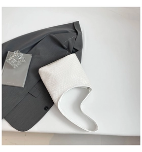 Detail of white woven hobo bag with leather texture placed next to a grey blazer