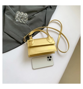 Detail of gold rectangular crossbody bag with handle and smartphone for size reference