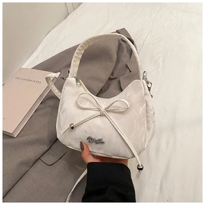 Detailed shot of white crescent bag with bow decoration and metallic brand logo