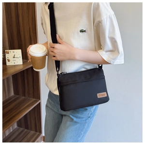 Close-up of black nylon crossbody bag featuring front zipper pocket and logo patch detail