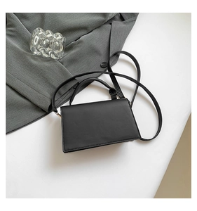 Flat lay of black matte leather square crossbody bag with gold buckle on white background