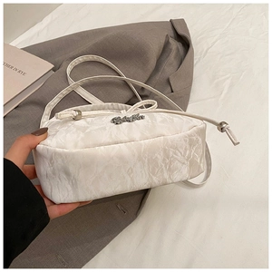 Detail of creamy white ruched shoulder bag featuring thin strap and metal logo accent