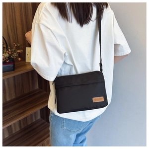 Close-up of black nylon crossbody bag featuring a brown leather logo patch on textured fabric