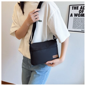Detail of minimalist black nylon crossbody bag with front zipper and fashion label
