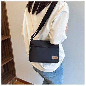 Side view of black nylon crossbody bag with adjustable strap and leather fashion logo