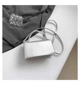 Detail of silver metallic square handbag featuring gold hardware and a top handle
