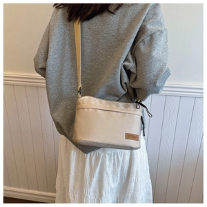 Close-up of a beige nylon crossbody bag with adjustable strap and front fashion logo