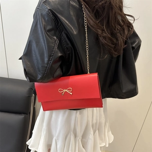 Chic red square shoulder bag with gold bow clasp and metal chain on a female model