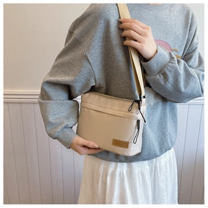Beige canvas crossbody bag with wide strap worn by a model in a soft lifestyle setting