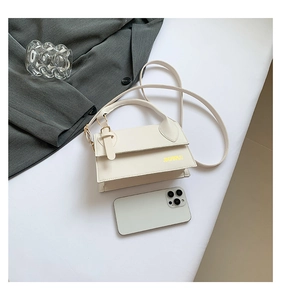 Detail of a creamy white square crossbody bag with gold lettering and top handle design