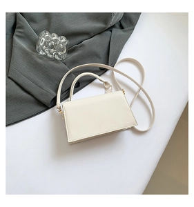Detail of a modern cream-colored square crossbody bag with gold hardware on flat surface
