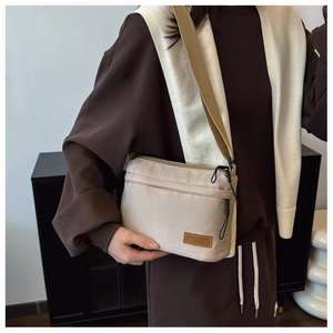 Détail du sac bandoulière en nylon beige avec double fermeture éclair et logo en cuir