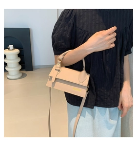 Detail view of a beige minimalist crossbody bag featuring a golden logo and top handle