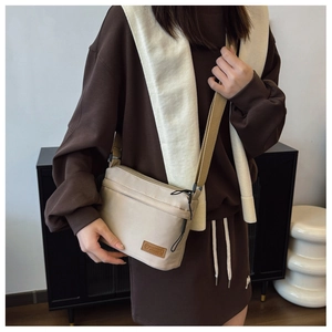 Détail du sac bandoulière en nylon avec poches zippées et écusson logo mode en cuir