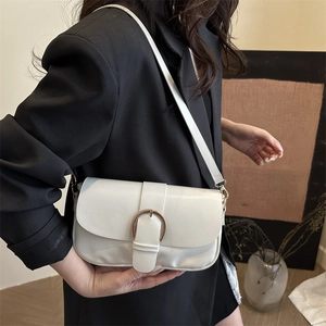 Détail d'un sac à bandoulière blanc minimaliste avec une boucle dorée en fer à cheval