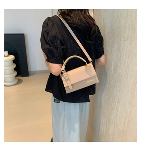 Rear view of a stylish beige crossbody bag with gold hardware on a modern female model