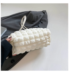 Detail of white bubble textured pleated shoulder bag on a grey blazer and book