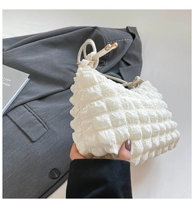 Detail shot of white popcorn textured handbag with pleated fabric and metal handle link