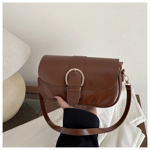 Détail d'un sac bandoulière en cuir brillant marron avec boucle fer à cheval dorée