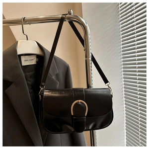 Détail du sac bandoulière en cuir ciré noir avec boucle fer à cheval dorée sur costume